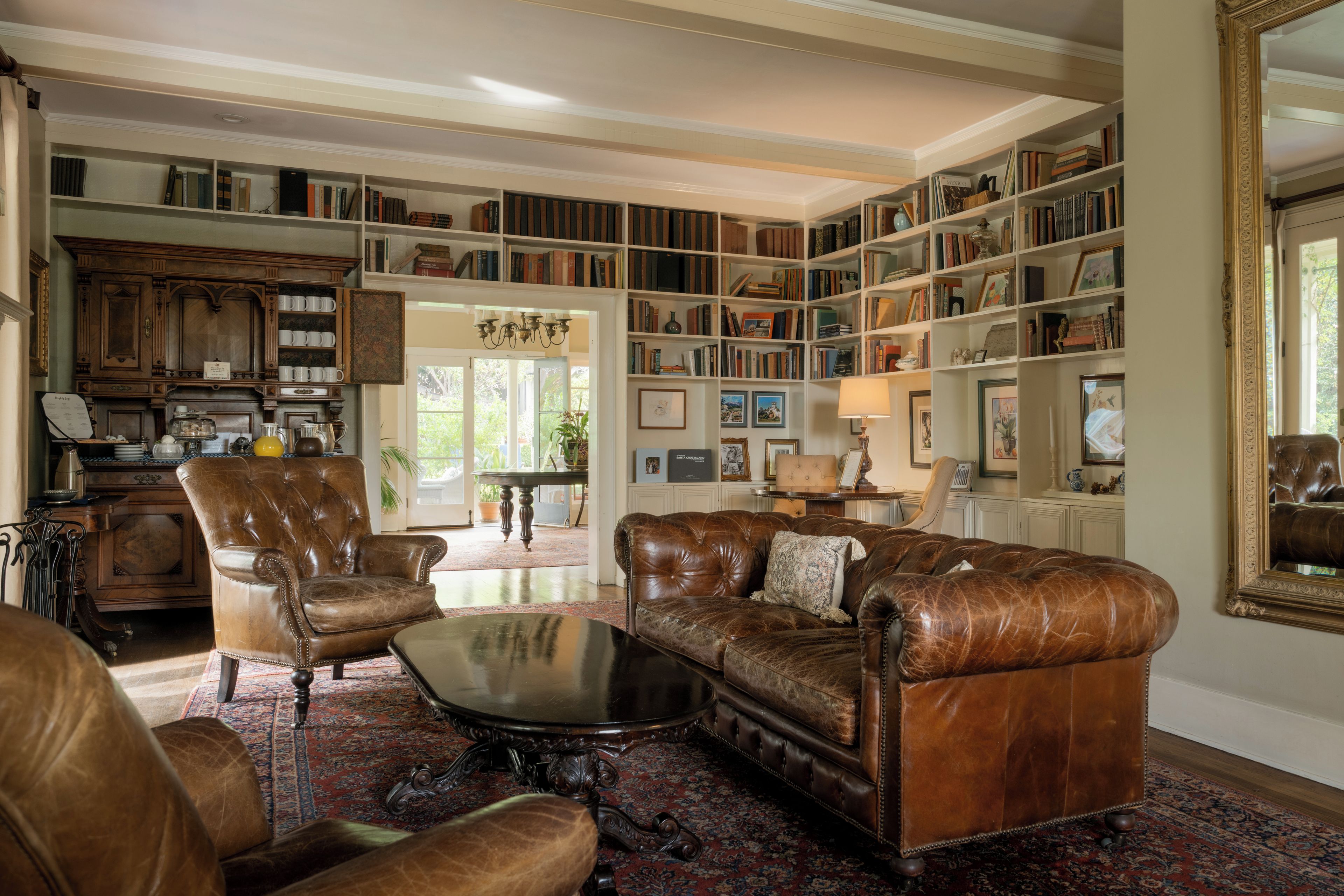 Een ruime woonkamer met lederen meubels, een grote boekenkast vol boeken en een eethoek met een tafel en stoelen.