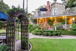 A two-story house with a balcony, a garden, and a wooden pergola.