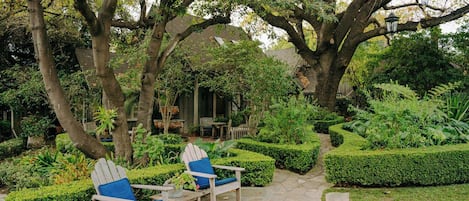 A garden with a stone pathway, two Adirondack chairs, and a wooden table.