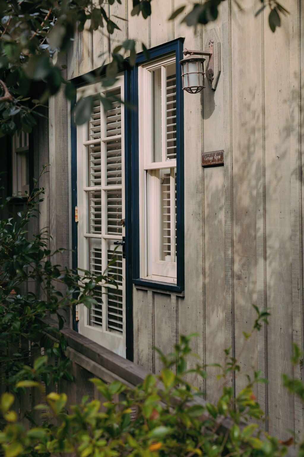 Un edificio de madera con dos ventanas, una con contraventanas y un letrero que indica una habitación tipo cabaña.