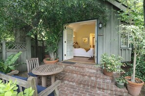 A wooden deck with a brick pathway leading to a bedroom with a bed and a nightstand.
