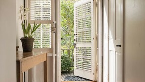 A hallway with wooden flooring, a patterned rug, a potted plant, and a door leading to an outdoor area with greenery. - Simpson House Inn (Santa Barbara)