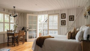 A bedroom with a bed, a dining table with chairs, a chandelier, and a view through a door.