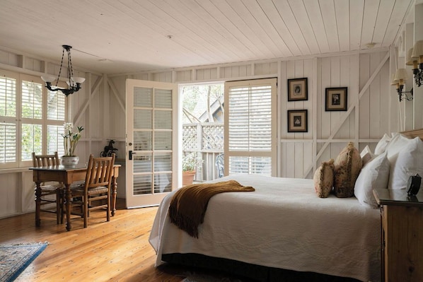 A bedroom with a bed, a dining table with chairs, a chandelier, and a view through a door. - Simpson House Inn (Santa Barbara)