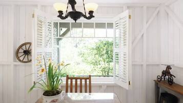 A dining area with a table, chairs, a chandelier, a window with shutters, and a decorative wheel.