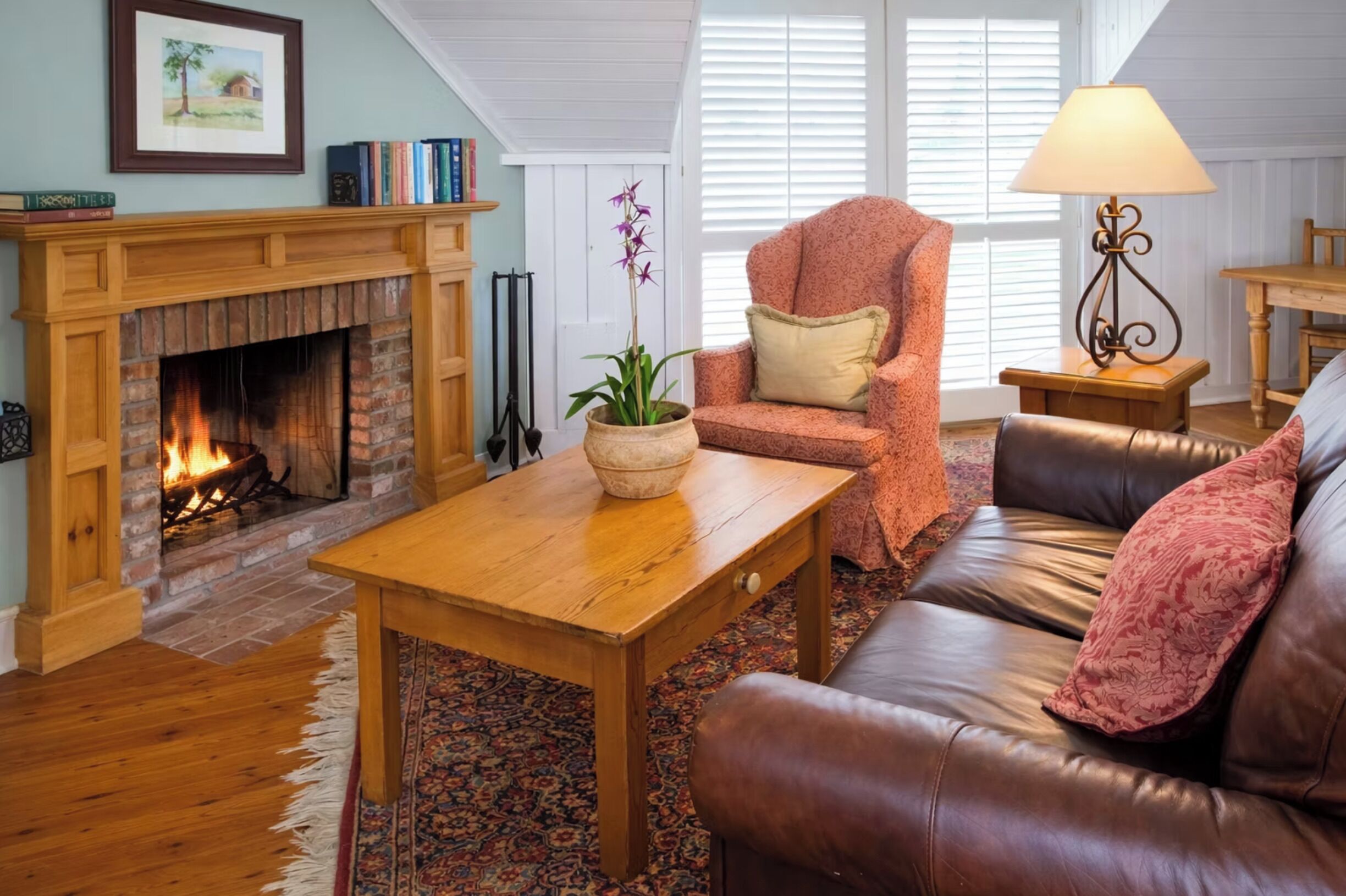 A cozy living room with a fireplace, leather sofa, wooden coffee table, and a potted plant.