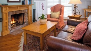 A cozy living room with a fireplace, leather sofa, wooden coffee table, and a potted plant.