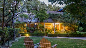 A house with a well-maintained garden, two wooden Adirondack chairs, and a lit interior. - Simpson House Inn (Santa Barbara)