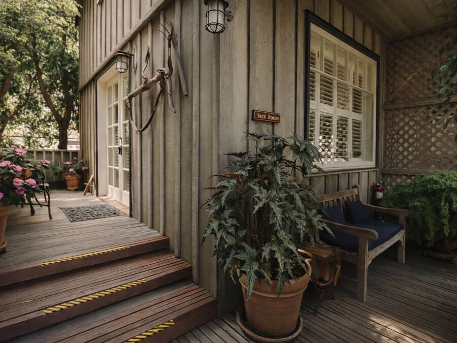 A wooden porch with steps leading to a door marked 'Tack Room,' a bench, and potted plants.