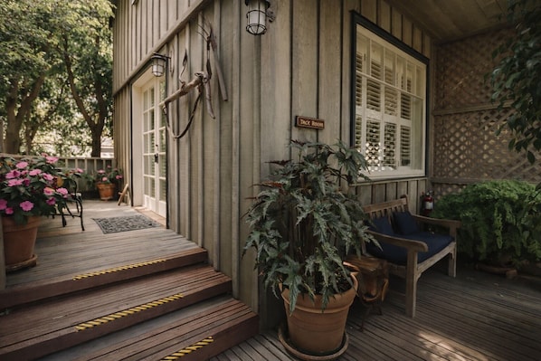 A wooden porch with steps leading to a door marked 'Tack Room,' a bench, and potted plants.