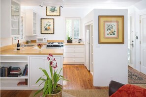 A modern kitchen with white cabinetry, a wooden countertop, and a gas stove. There are framed botanical prints on the walls, and a potted orchid on the counter.