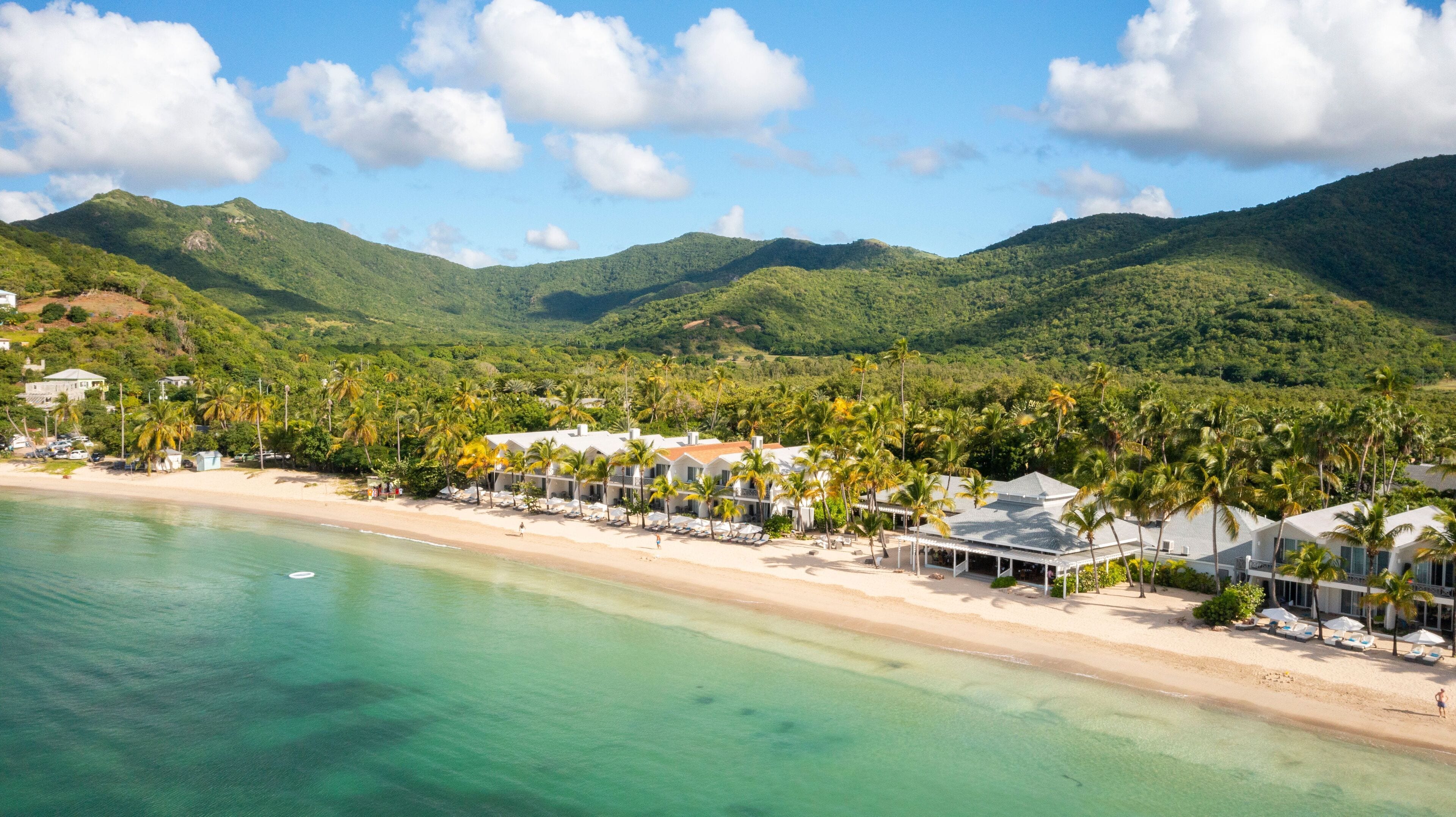 A coastal resort with beachfront villas, palm trees, and a mountainous backdrop.