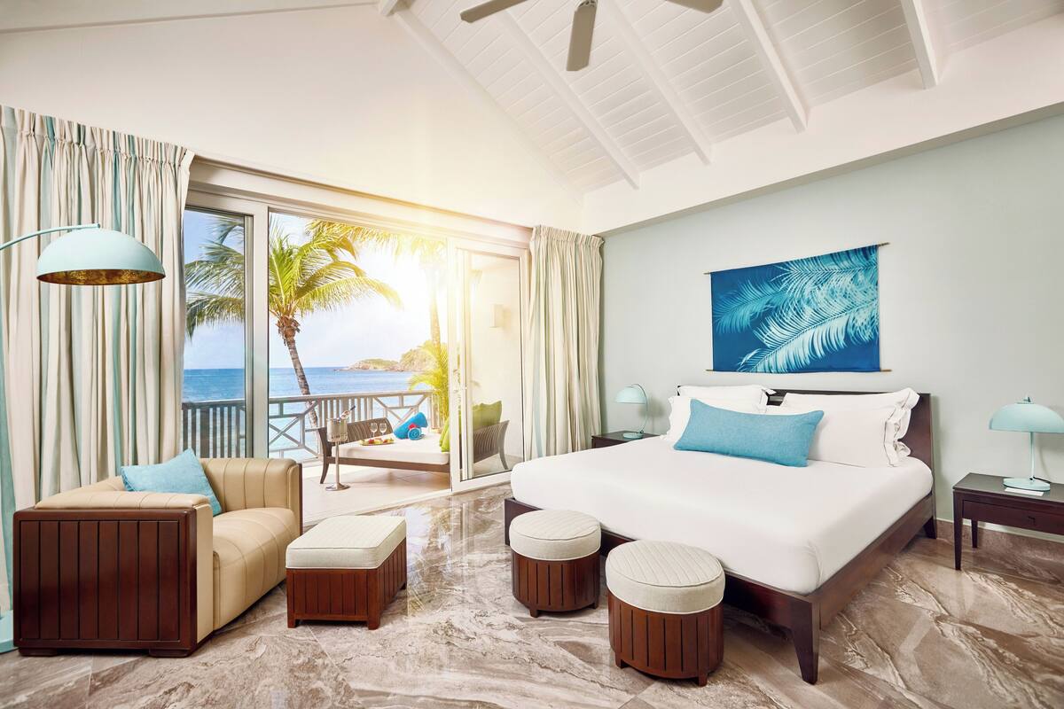 A hotel room with a large bed, a sofa, and a balcony with a view of the ocean.