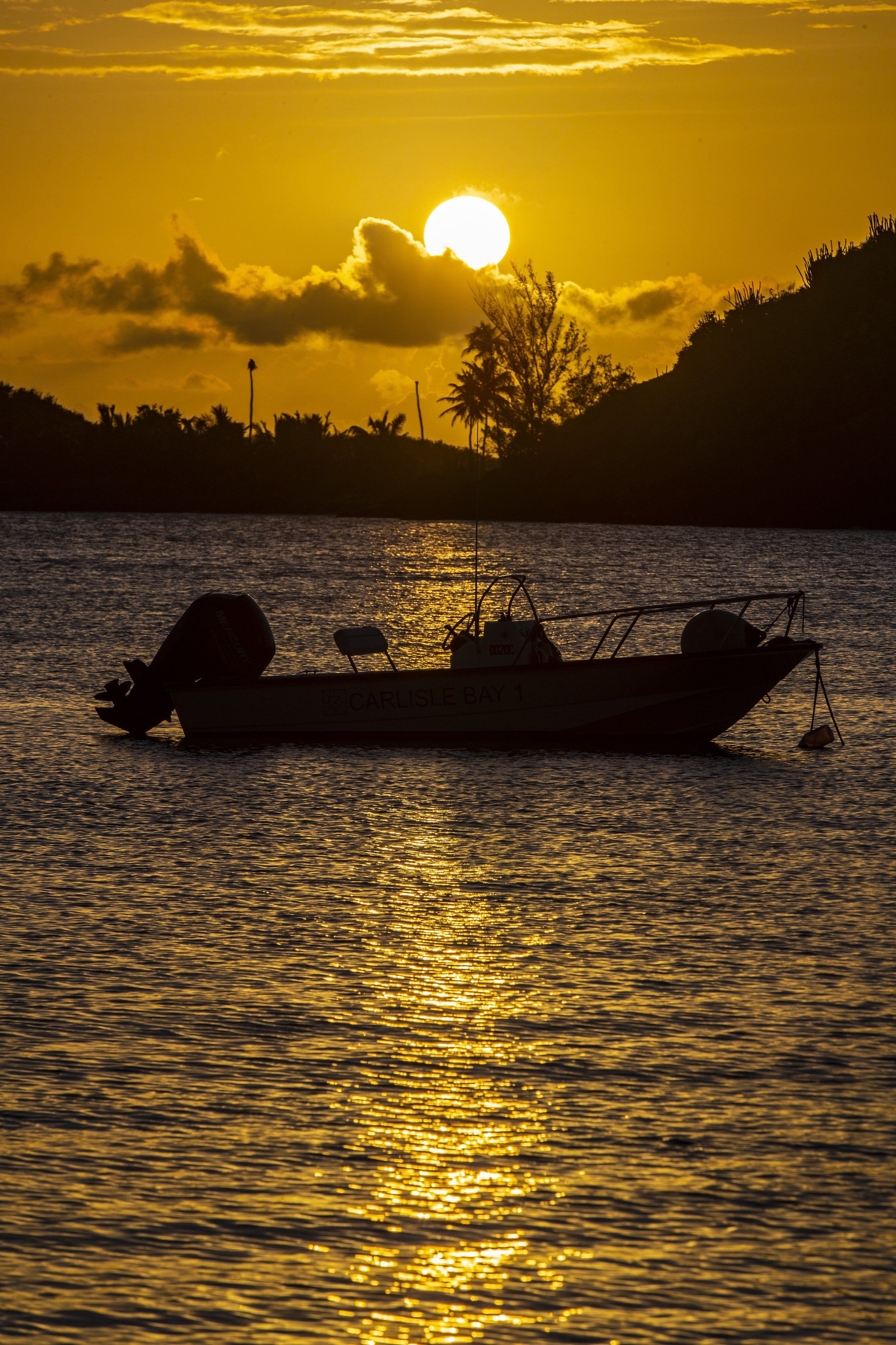 A boat named "RECARLIS BAY 1" on calm water during sunset.