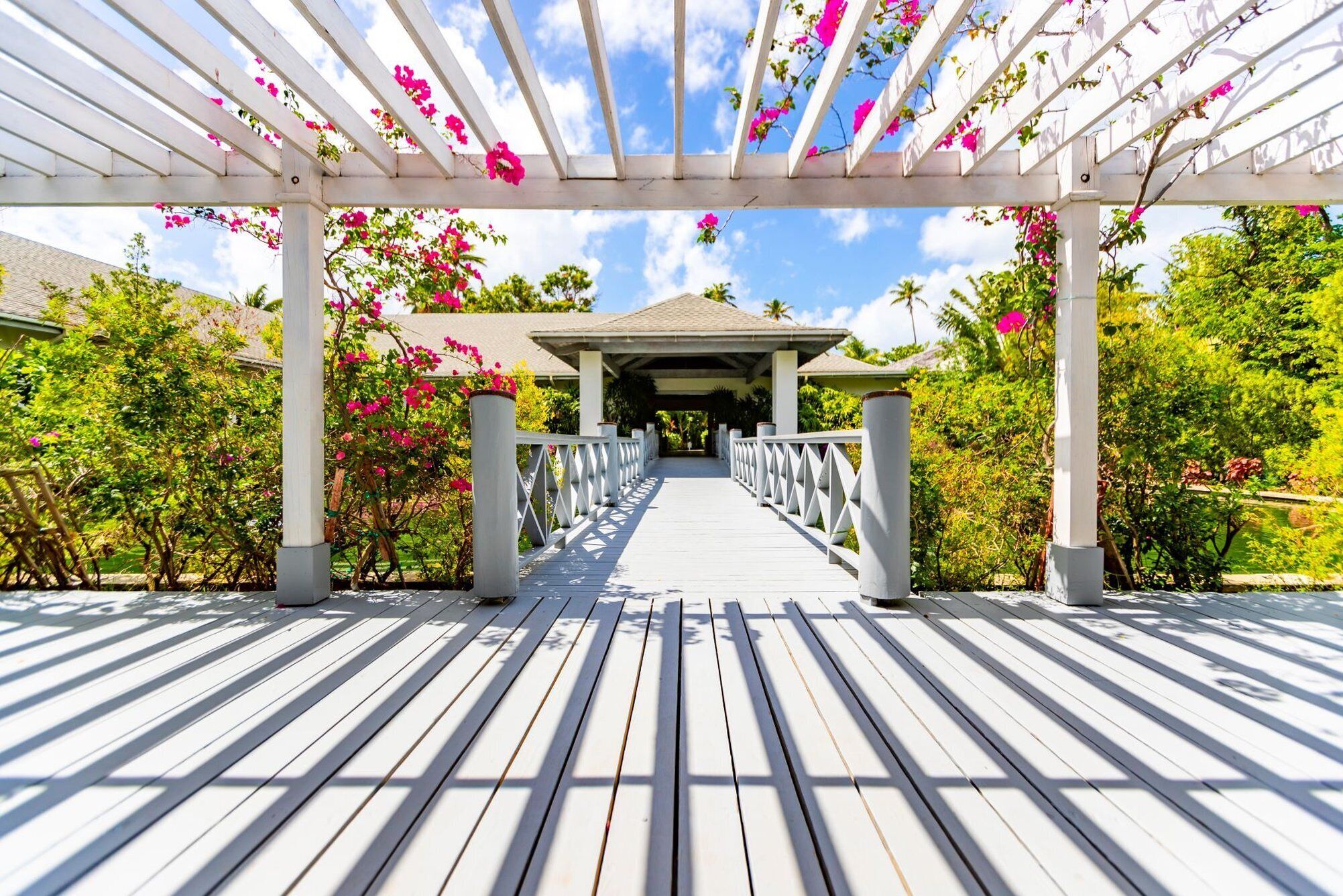 A wooden deck leading to a covered pavilion with a view of lush greenery and a clear sky.