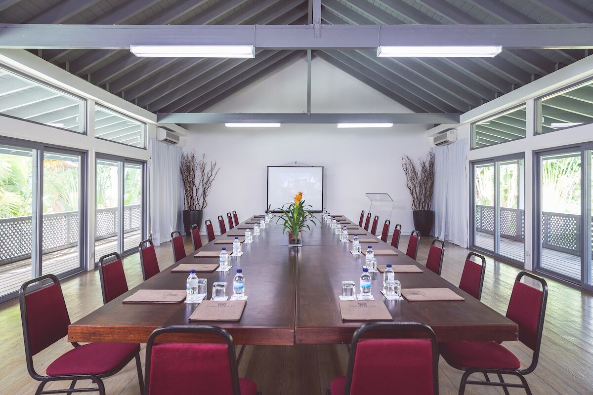 A conference room with a long table, red chairs, water bottles, and a projector screen.