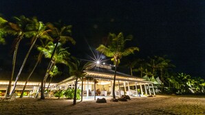 A beachfront hotel with a covered outdoor seating area, palm trees, and a starry night sky. - Carlisle Bay (Carlisle Bay)