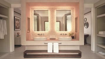 A modern bathroom with a large mirror, two sinks, and a bench.