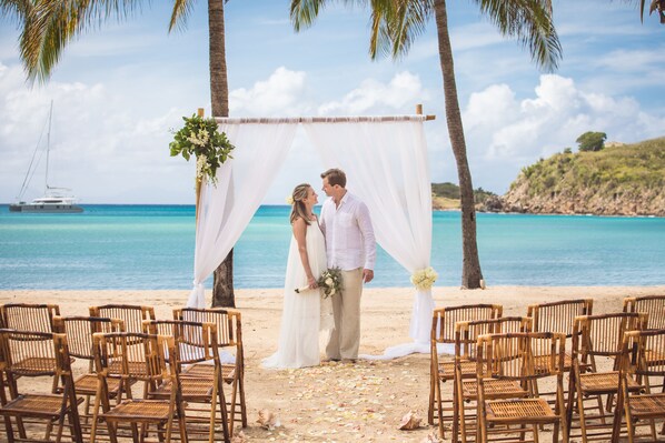 A beach wedding ceremony with a white arch and wooden chairs. - Carlisle Bay (Carlisle Bay)
