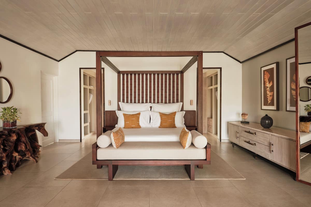A spacious bedroom with a four-poster bed, a wooden headboard, and a large mirror on the wall.