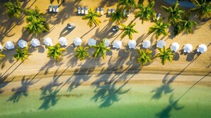 An aerial view of a beach with rows of white umbrellas and lounge chairs, surrounded by palm trees. - Carlisle Bay (Carlisle Bay)