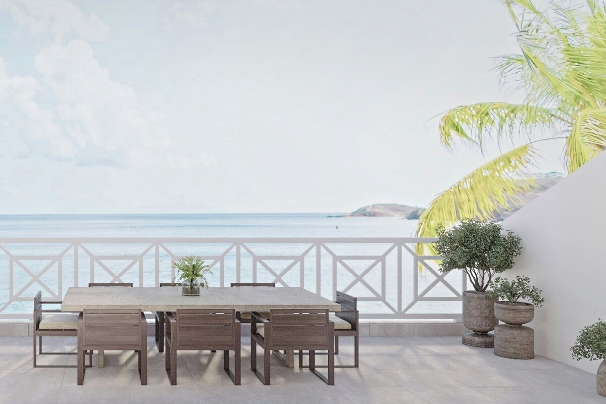 A terrace with a view of the sea, a table with chairs, and potted plants.