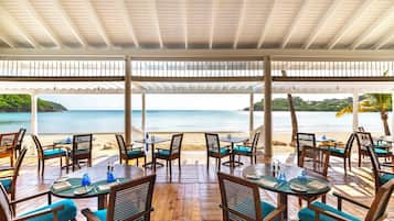 An outdoor dining area with tables and chairs, overlooking a beach and the ocean.