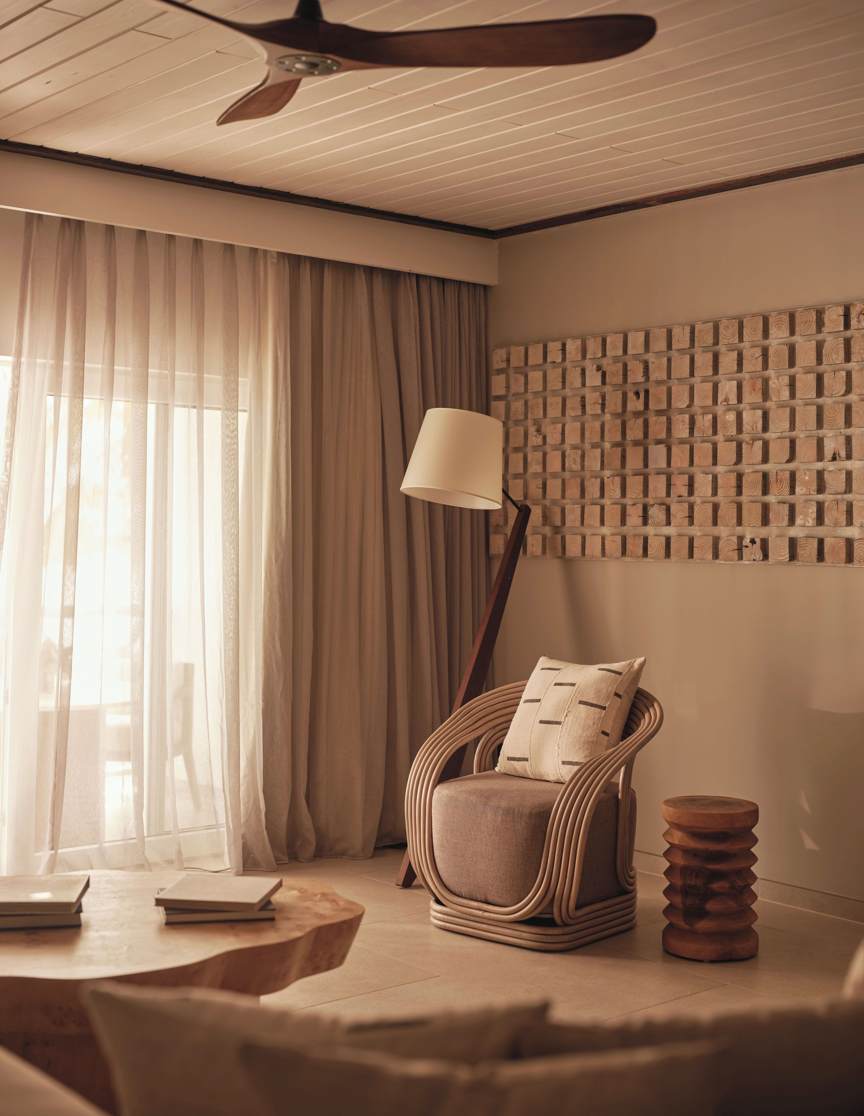 A room with a ceiling fan, a wicker chair with a cushion, a floor lamp, and a wall with a patterned design.