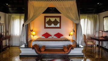 Un dormitorio con cama a dosel, dos almohadas rojas, un banco de madera, un escritorio y una lámpara.