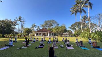 Un grupo de personas practicando yoga sobre esterillas en un espacio al aire libre, con un edificio al fondo.