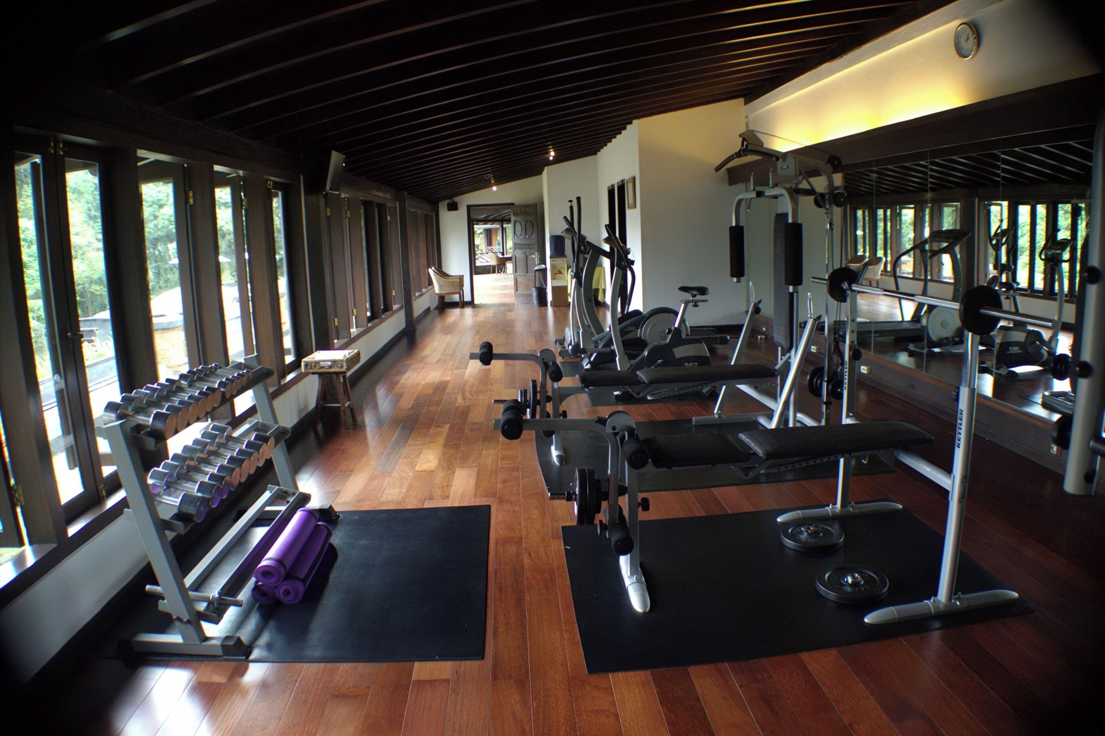 Una palestra con attrezzature per esercizi, pavimenti in legno e ampie finestre.