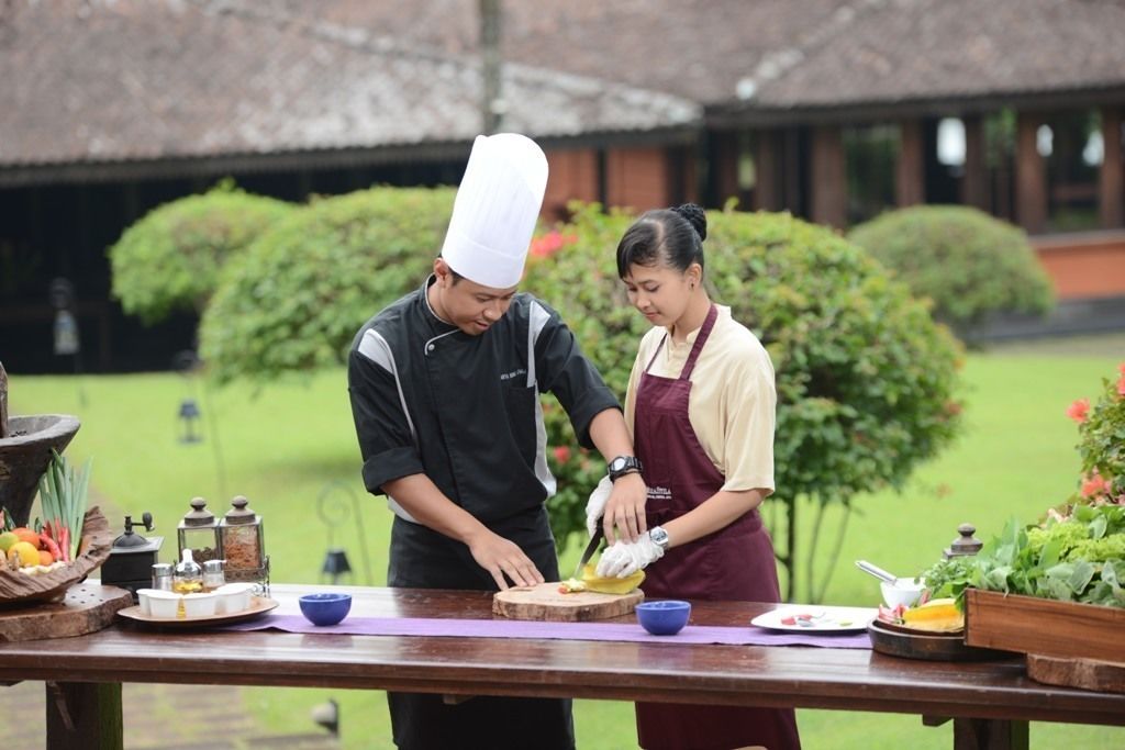 A chef and a server preparing food outdoors with a table set with various dishes and condiments.