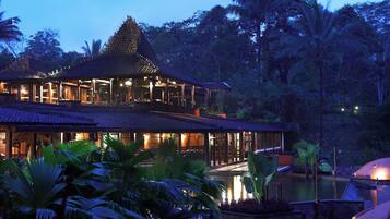 A two-story resort with a pool, surrounded by tropical vegetation.