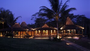 A traditional-style building with multiple roofs, surrounded by palm trees and a well-lit pathway. - MesaStila Resort and Spa (Pringsurat)