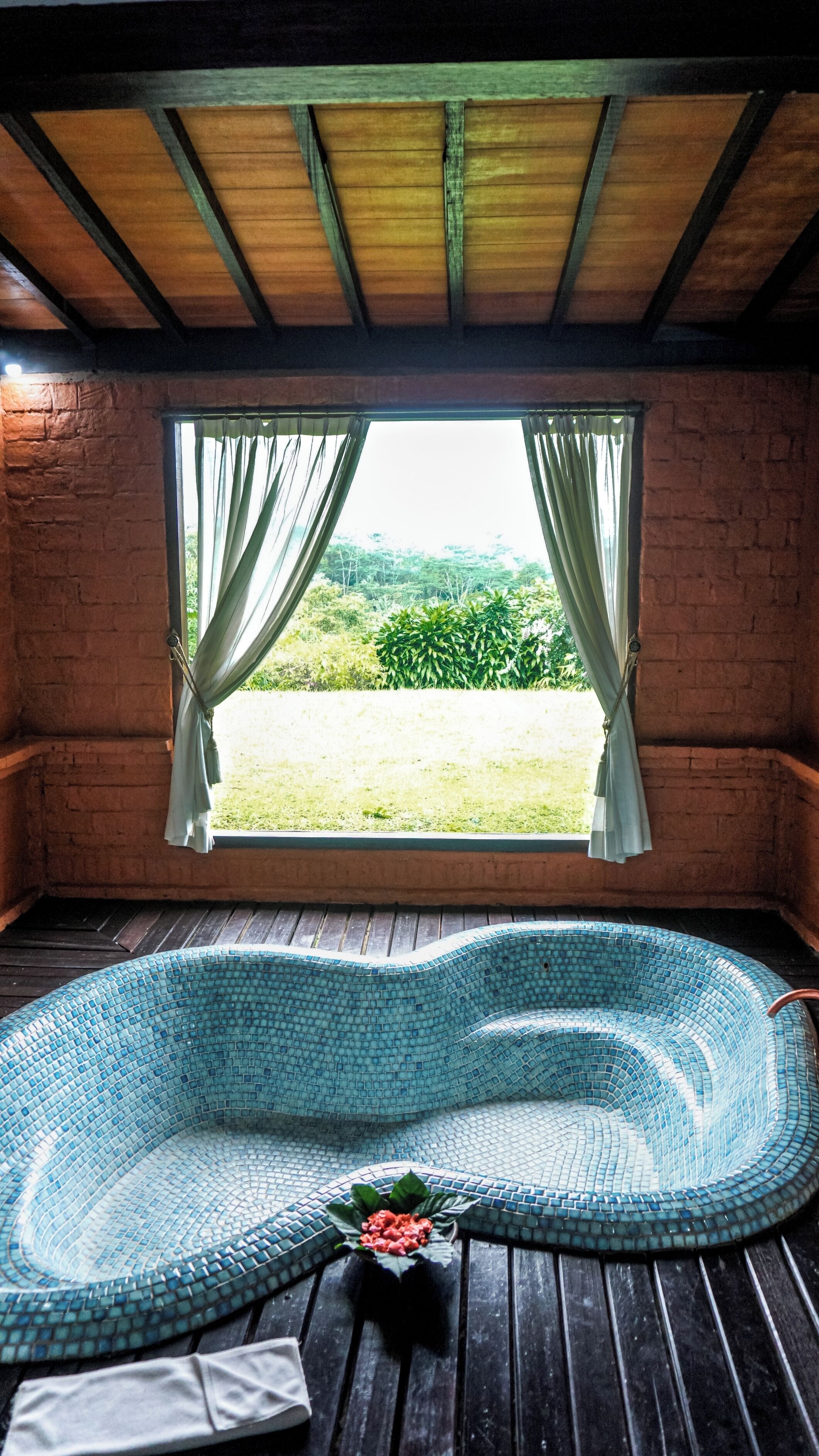 A room with a large window, a wooden bench, and a small table with a flower.