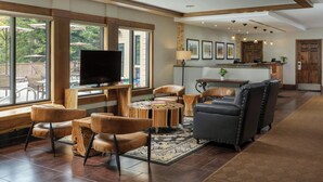 A spacious living area with a large flat-screen TV, leather sofas, a coffee table, and a view of the outdoors through large windows. - Marriott's StreamSide Birch at Vail (Vail)