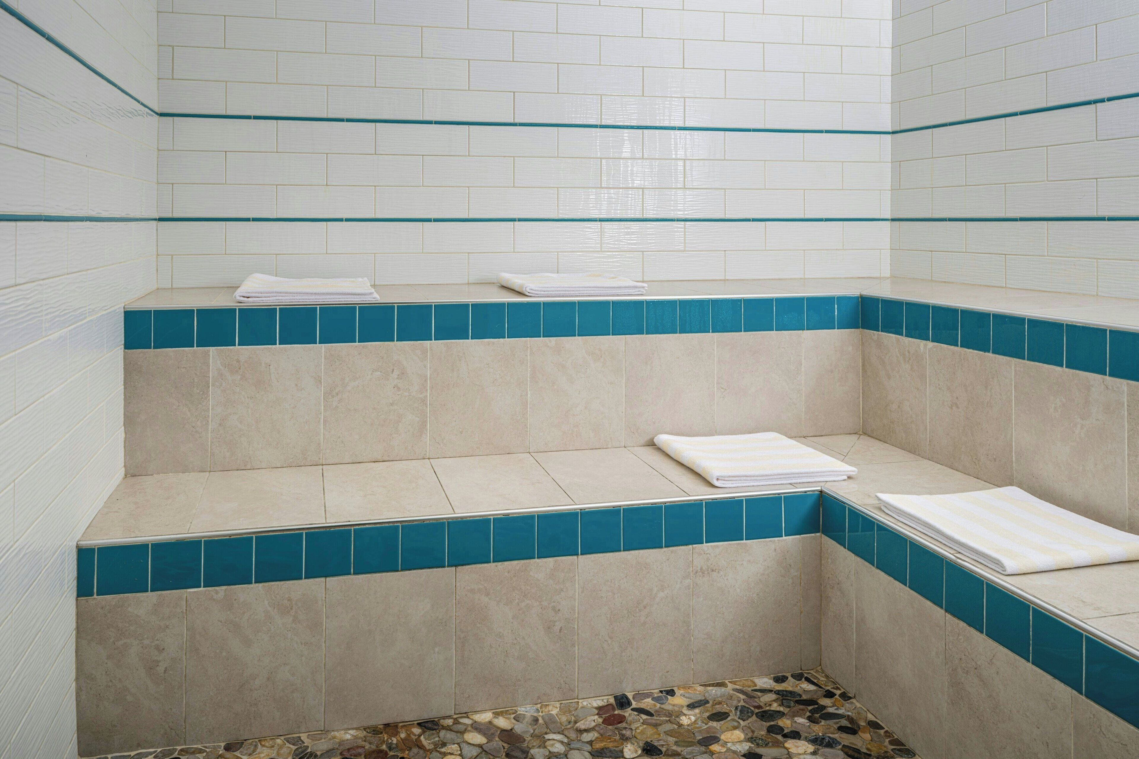 Un baño con azulejos blancos y azules, un banco y un piso de mosaico.