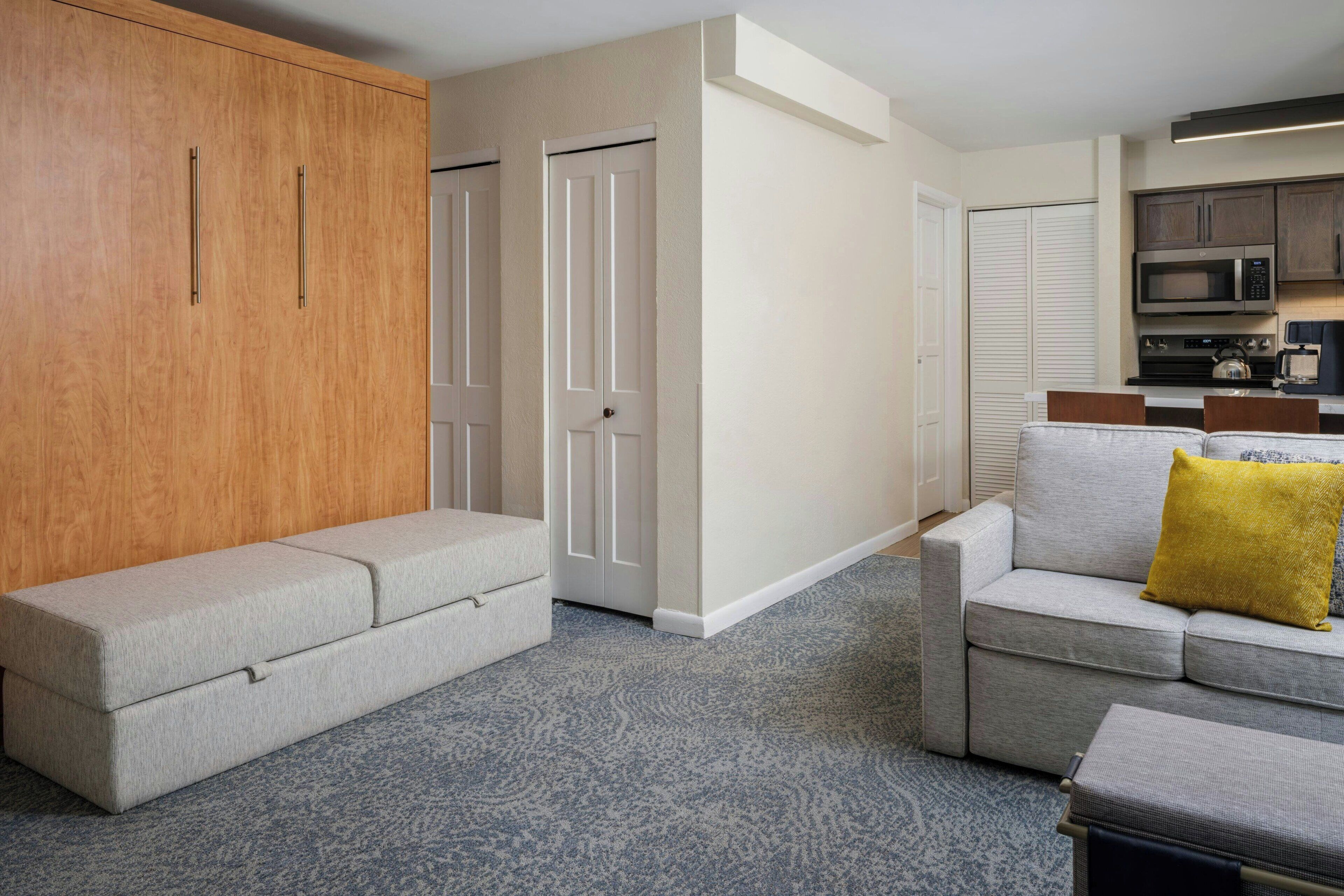 A modern living room with a grey sofa, a matching ottoman, and a wooden wardrobe.