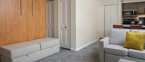 A modern living room with a grey sofa, a matching ottoman, and a wooden wardrobe.