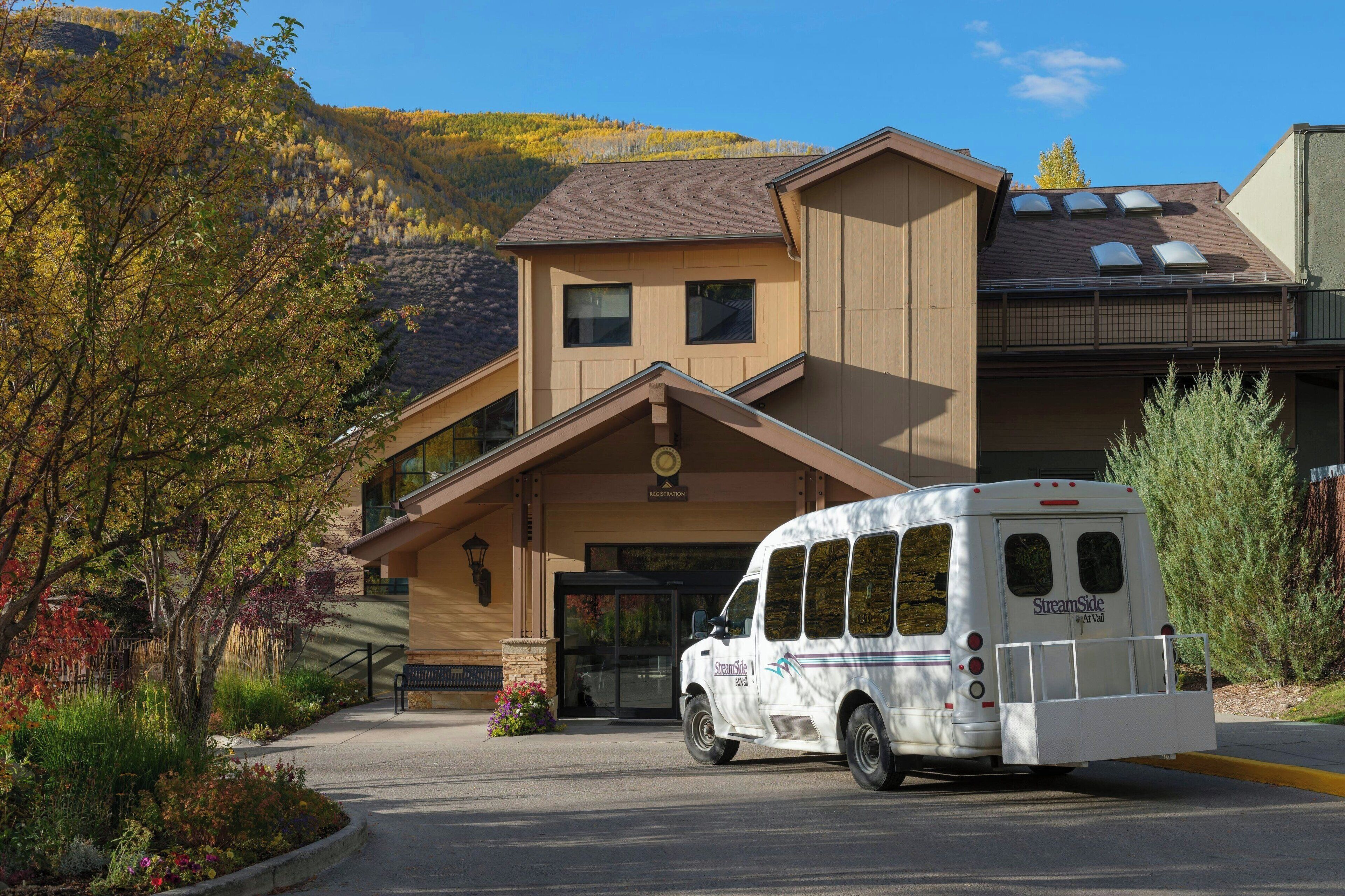 A building with a reception area, a van parked in front, and a mountainous backdrop.