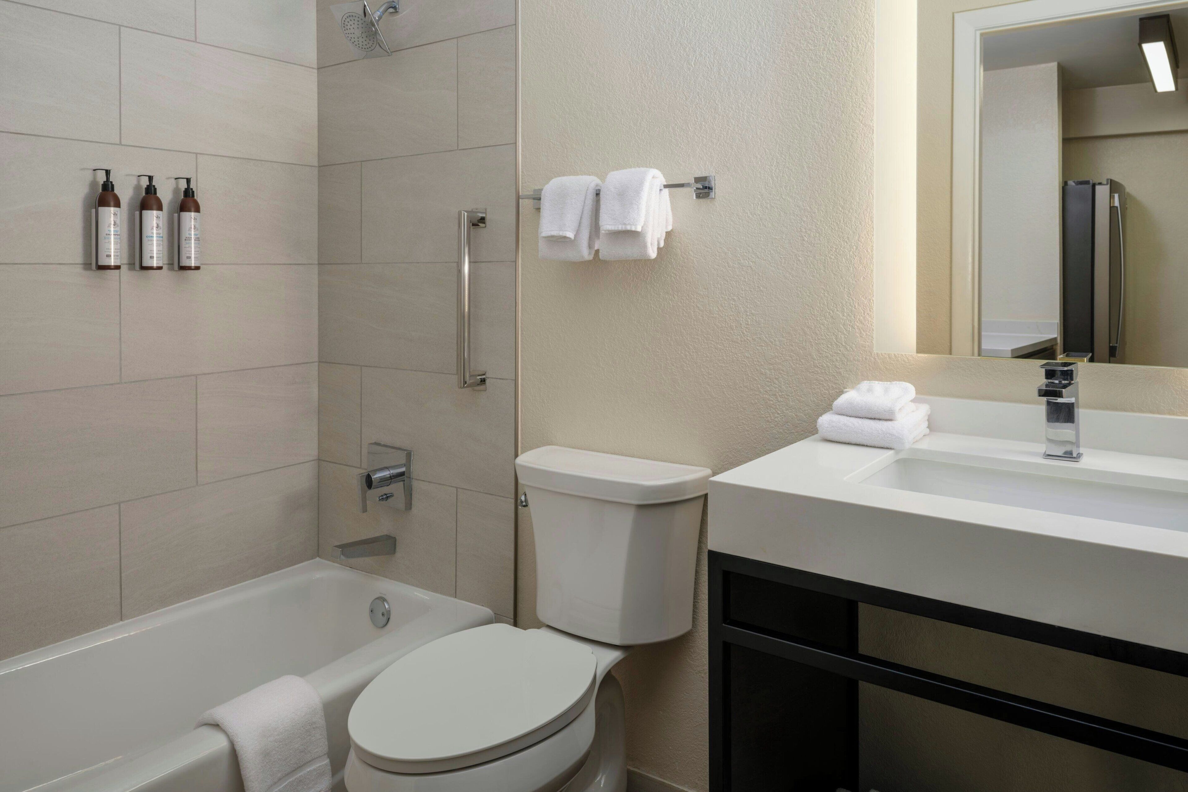 Un baño moderno con bañera, inodoro y lavabo. Hay artículos de aseo en la pared y toallas colgadas en un perchero.
