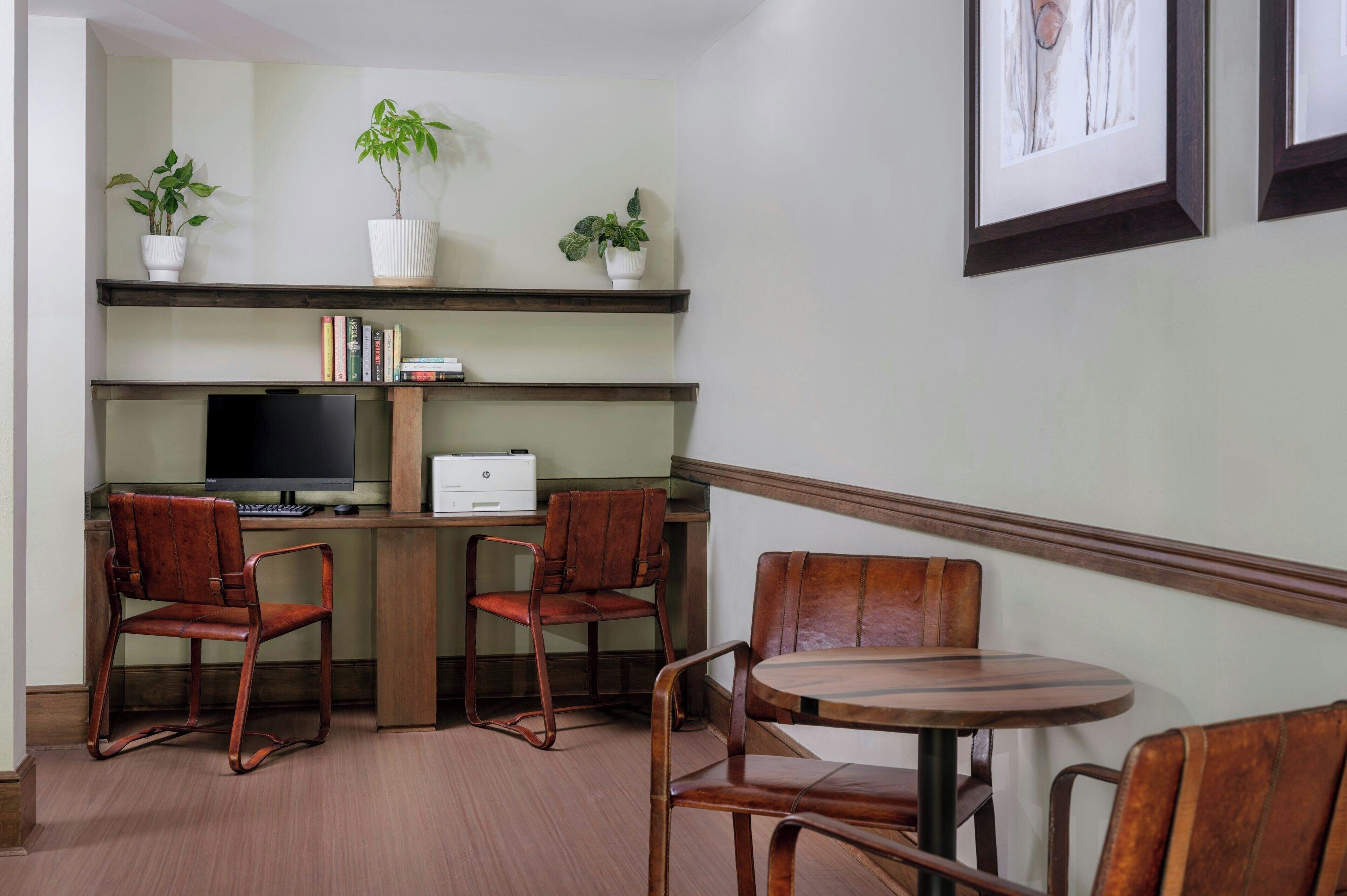 Una habitación con un escritorio, dos sillas, una mesa redonda, un televisor y tres plantas en macetas sobre estantes.