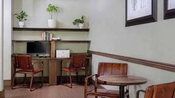 Una habitación con un escritorio, dos sillas, una mesa redonda, un televisor y tres plantas en macetas sobre estantes.