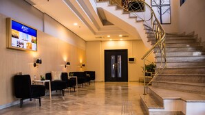 A modern hotel lobby with a marble floor, black chairs, a reception desk, a digital screen, and a staircase. - Blue Tree Towers Anália Franco - Tatuapé (São Paulo)