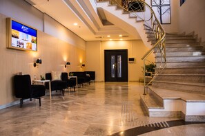 A modern hotel lobby with a marble floor, black chairs, a reception desk, a digital screen, and a staircase. - Blue Tree Towers Anália Franco - Tatuapé (São Paulo)