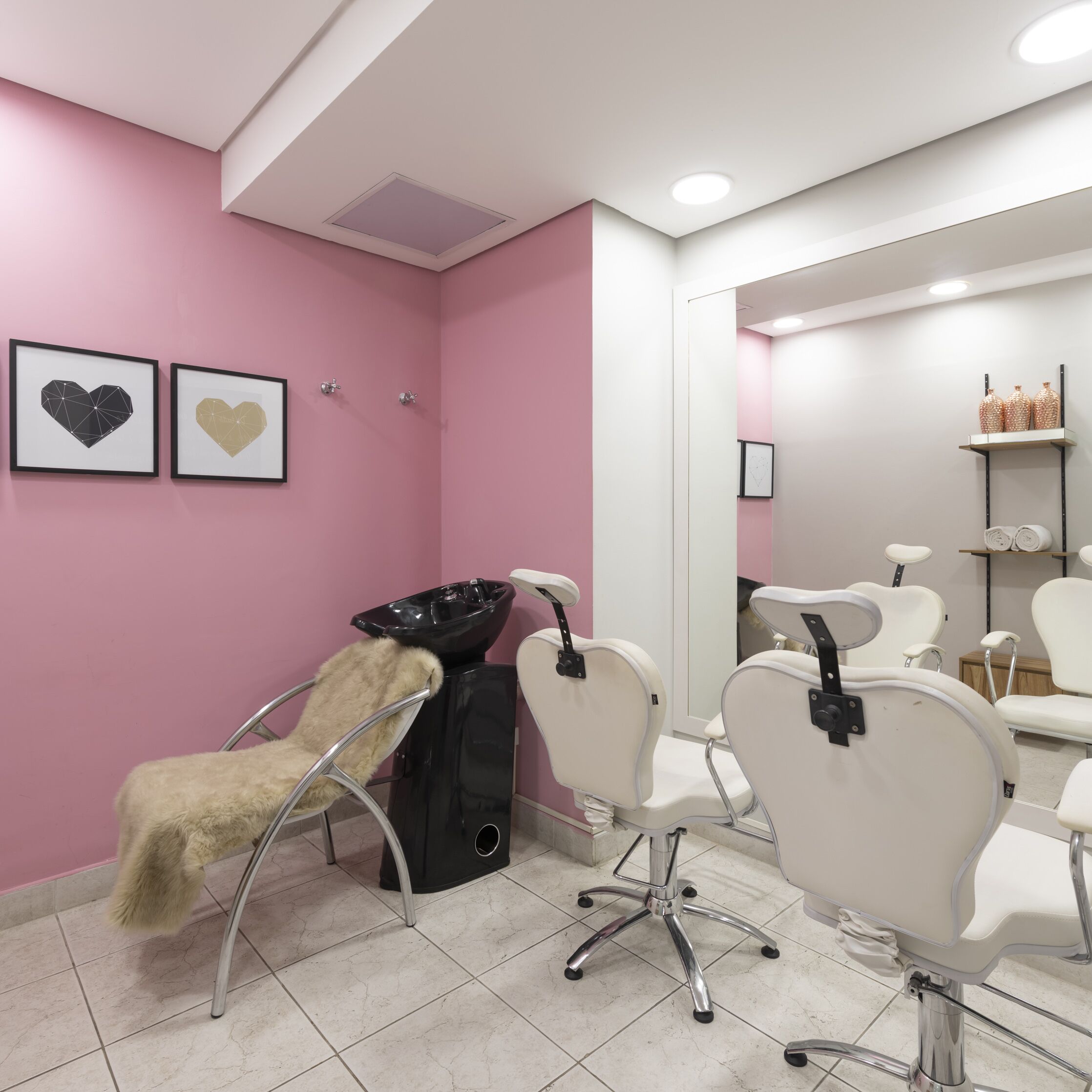 Ein moderner Friseursalon mit rosafarbenen Wänden, zwei gerahmten Herzmotiven und weißen Friseurstühlen.