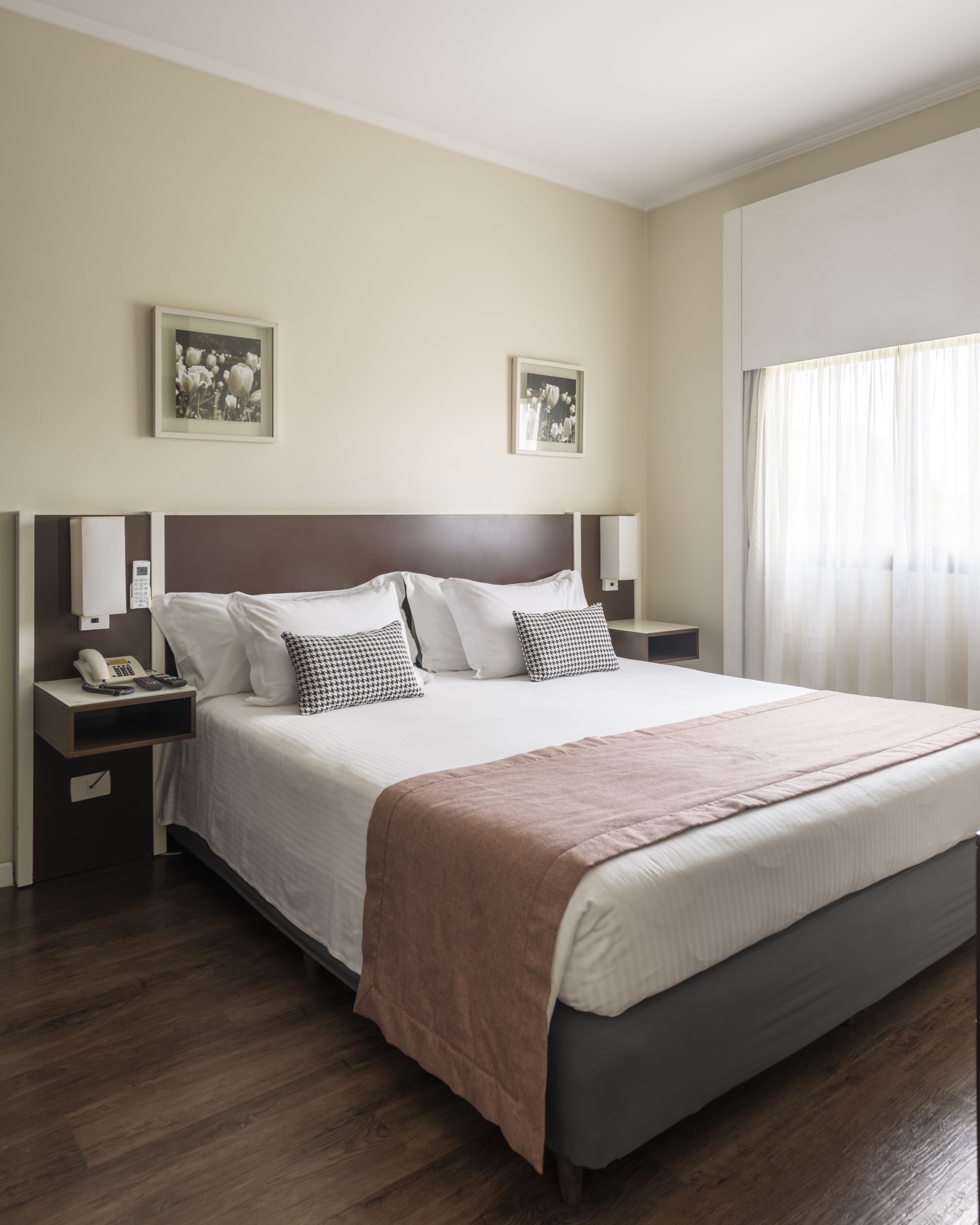 A hotel room with a large bed, two bedside tables, a nightstand, a telephone, and two framed pictures on the wall.