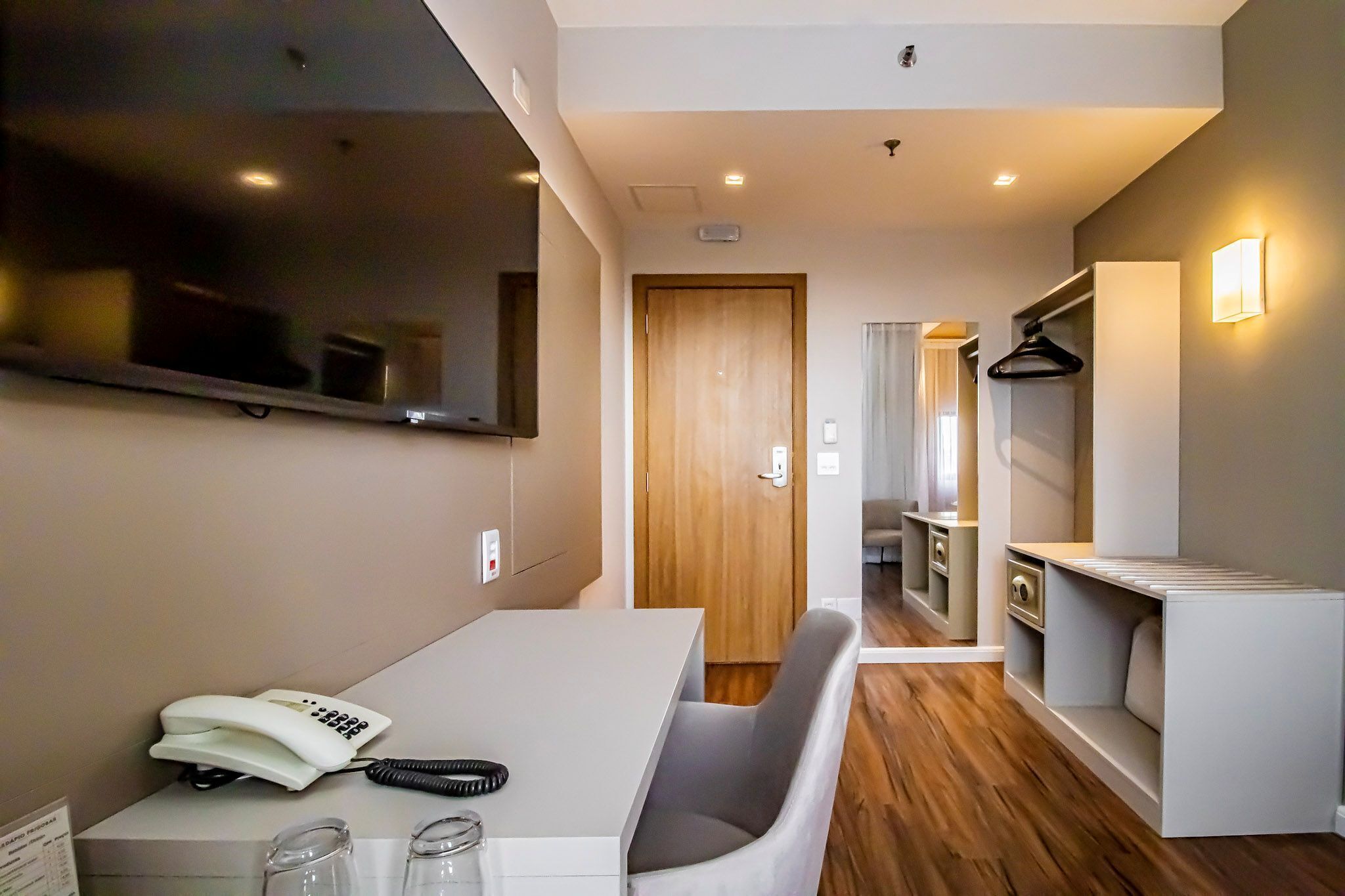 A hotel room with a flat-screen TV, a desk with a telephone, and a chair.