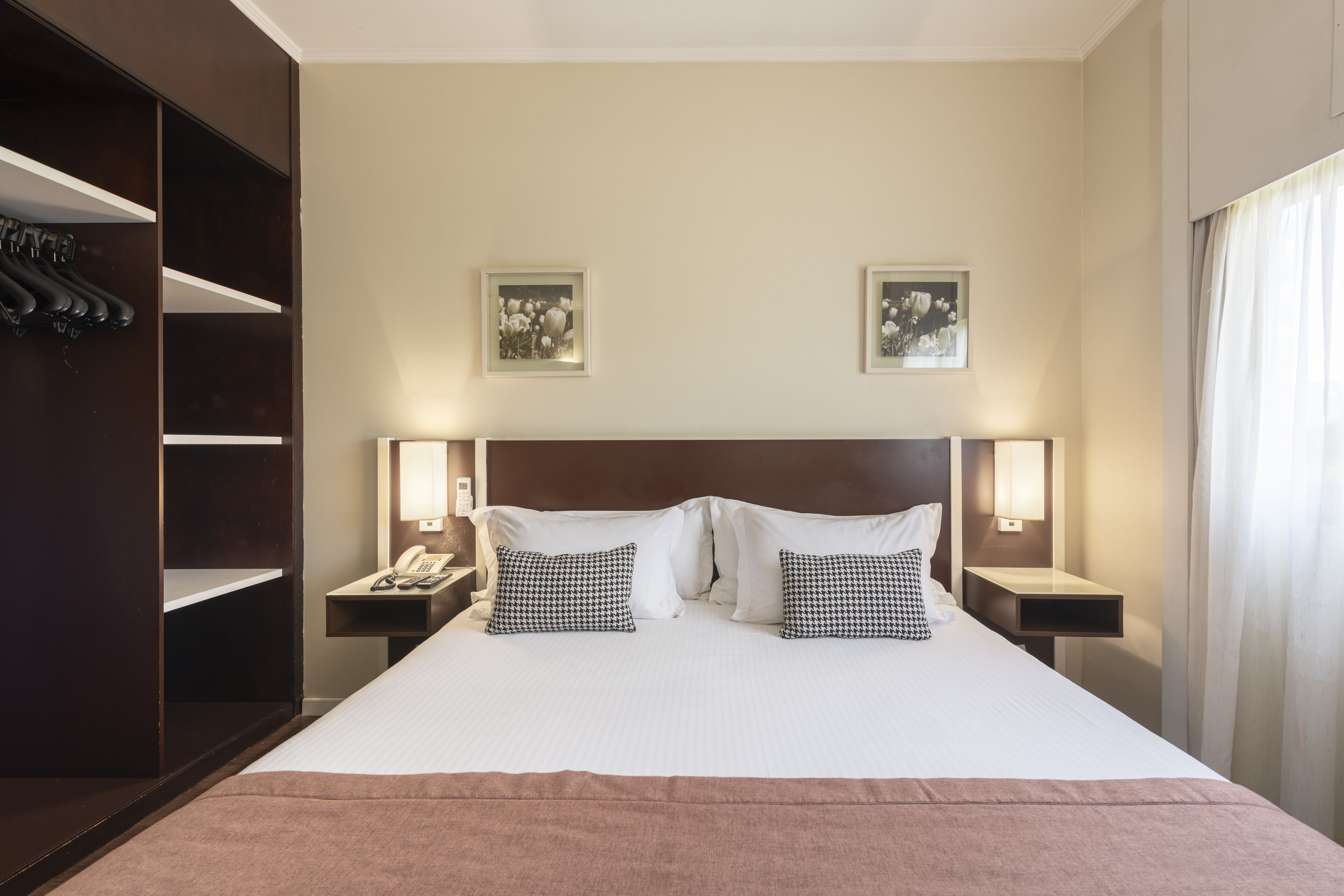 A hotel room with a large bed, two bedside tables, a wardrobe, and two wall-mounted lamps.