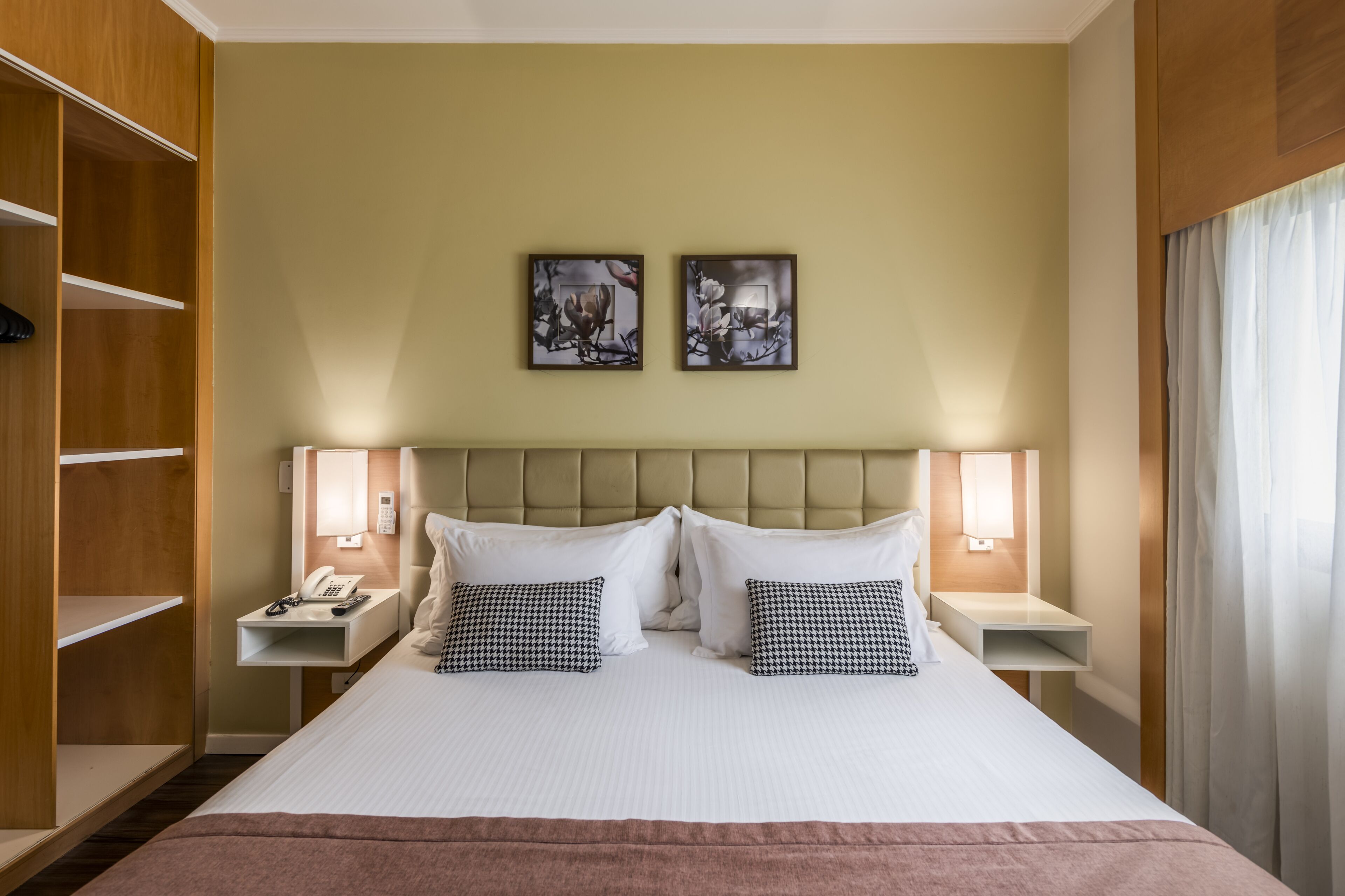 Une chambre d’hôtel avec un grand lit, deux tables de chevet avec des lampes, une armoire et deux œuvres d’art accrochées au mur.